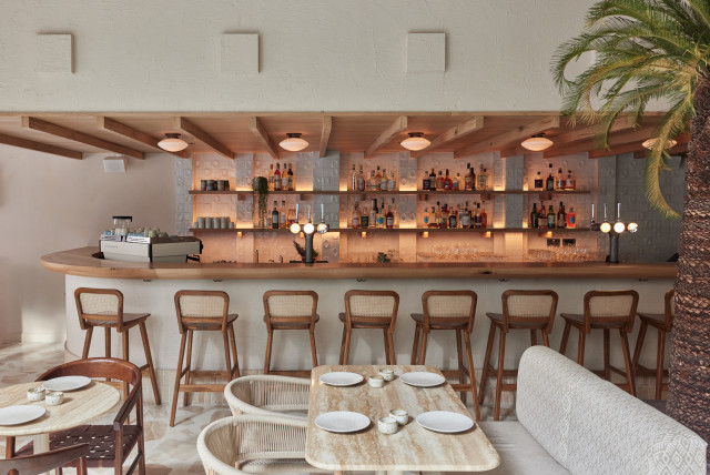 Bar counter lined with wooden stools, displaying bottles and glasses on shelves