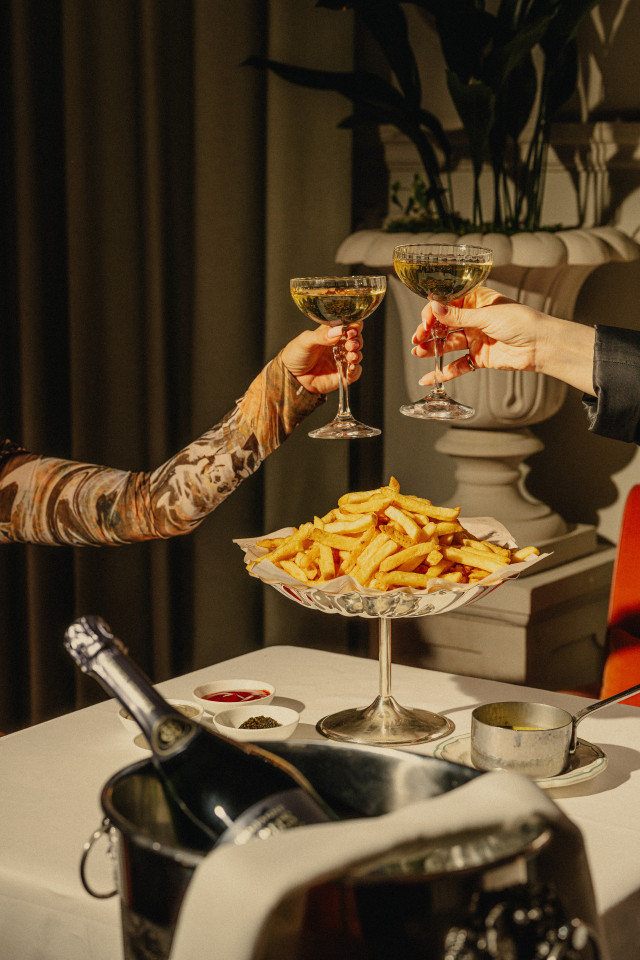 two people clinking glasses over dish of chips