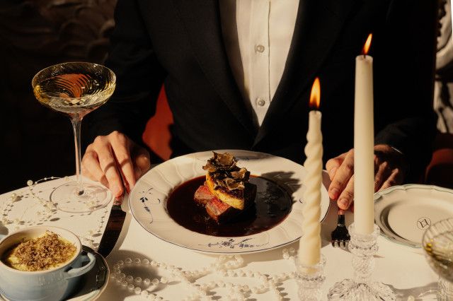 person sat at restaurant table in tuxedo with meat dish and glass of wine