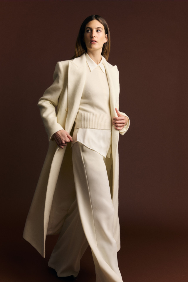 model wearing cream trouser suit, cream jumper and cream longline coat