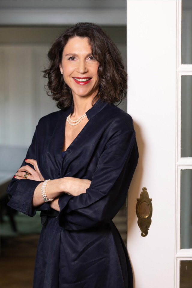 woman in blue dress smiling at camera with arms folded