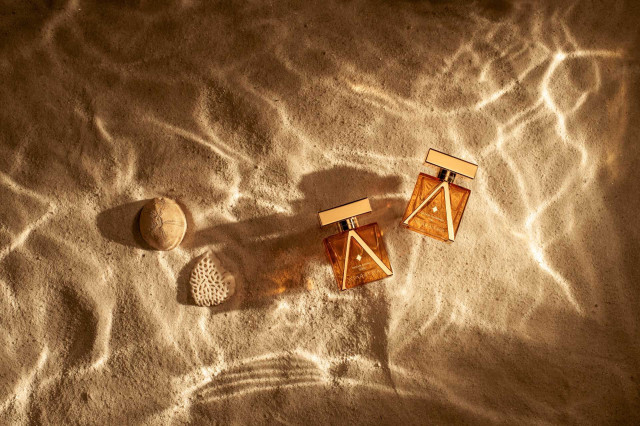 two perfume bottles lying on sand with water ripples over the top 
