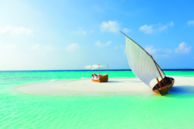 person sitting on bench in the maldives with boat on the sand