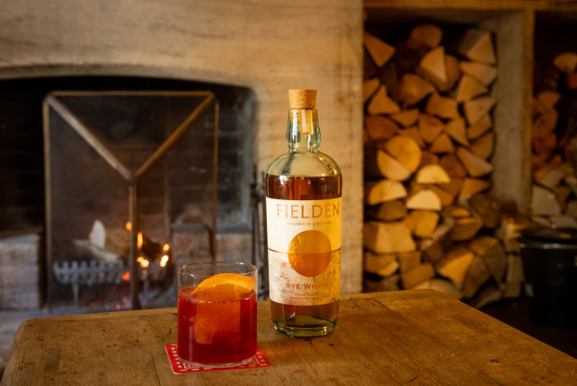 negroni on wooden table next to bottle of fielden whisky 