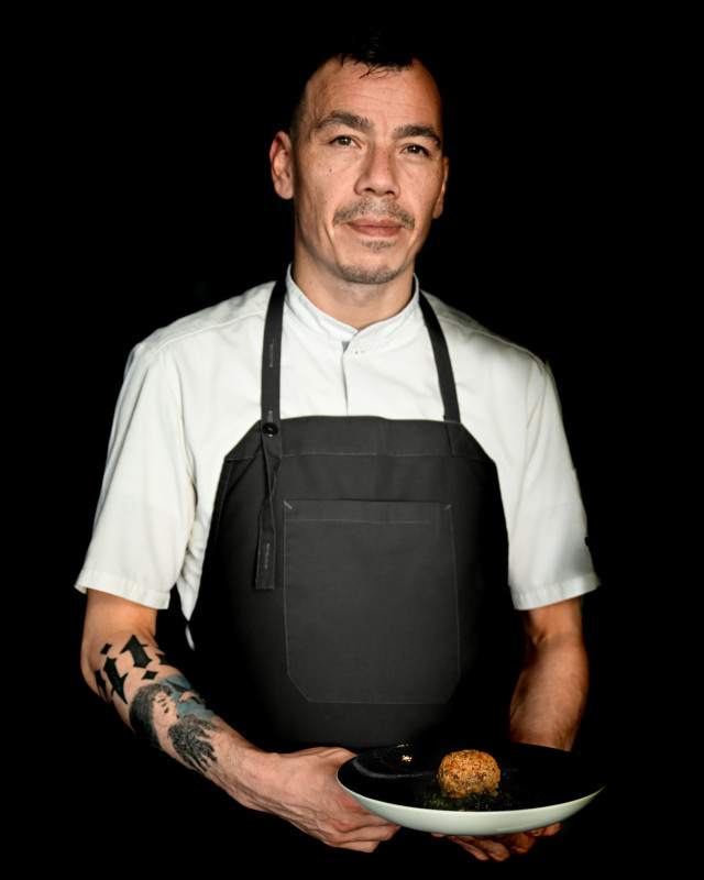 chef holding dish in dark apron and white shirt