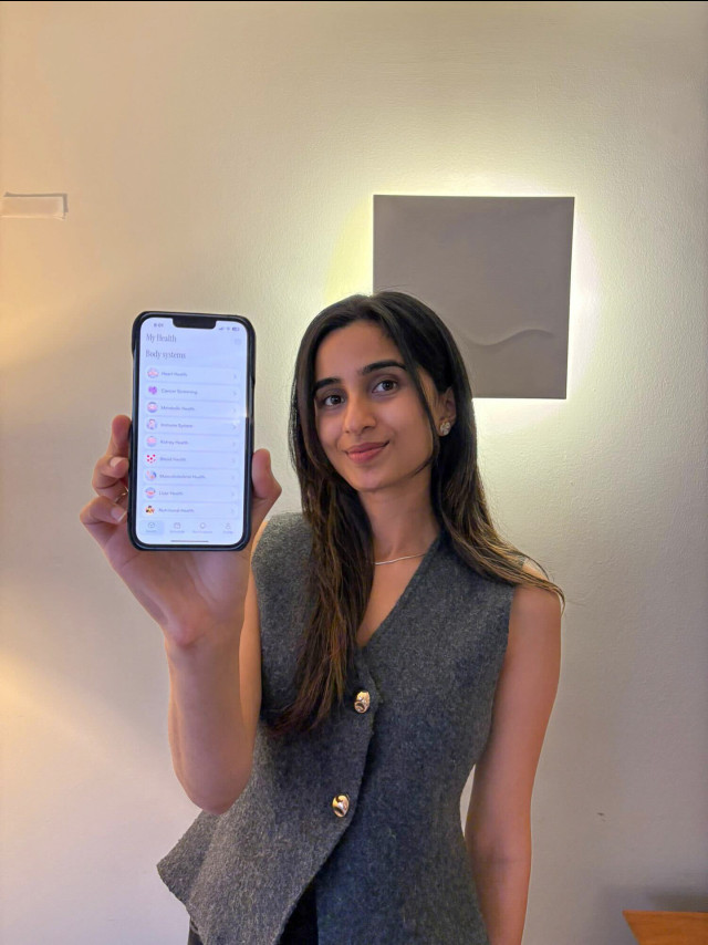 photo of woman in waistcoat holding phone with app displayed 
