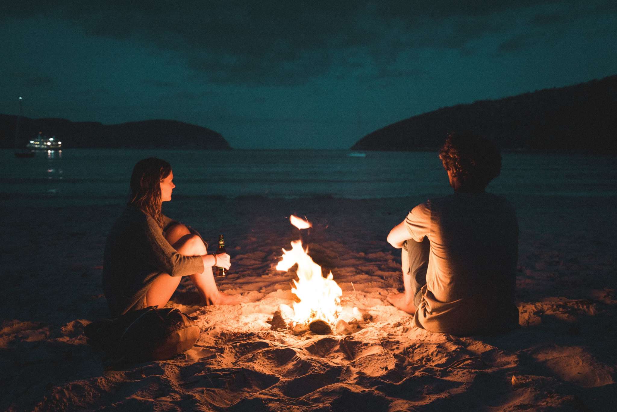 Couple sat at a campfire by the sea.