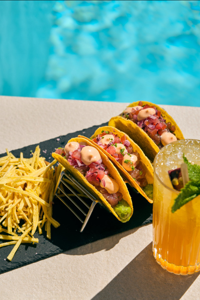 three fish tacos and fruit juice placed next to hotel pool