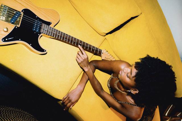 woman lying on yellow sofa next to wooden guitar