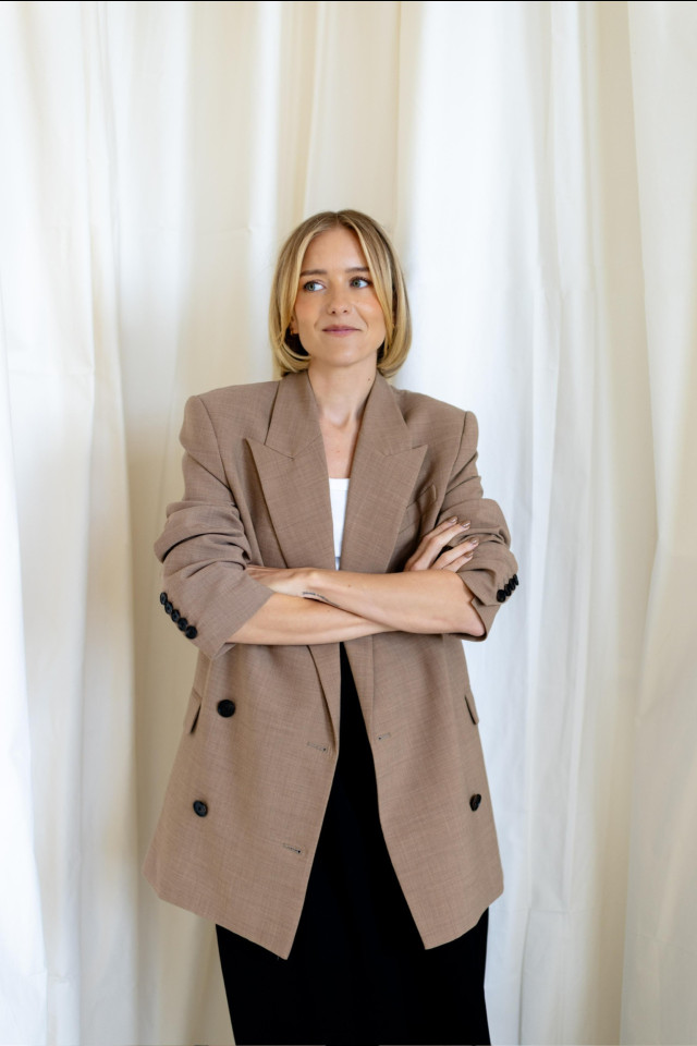 hermione olivia in a brown blazer with her arms crossed