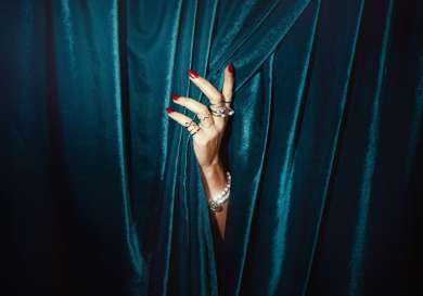 Model with hand poking through teal velvet curtains.