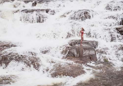 Adventurous woman standing on white water rocks.