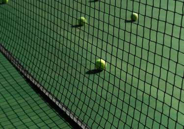 Green tennis court with yellow tennis balls on it.