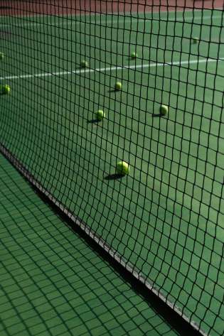 Green tennis court with yellow tennis balls on it.