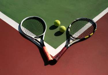 2 tennis rackets and 2 tennis balls sitting on a court.
