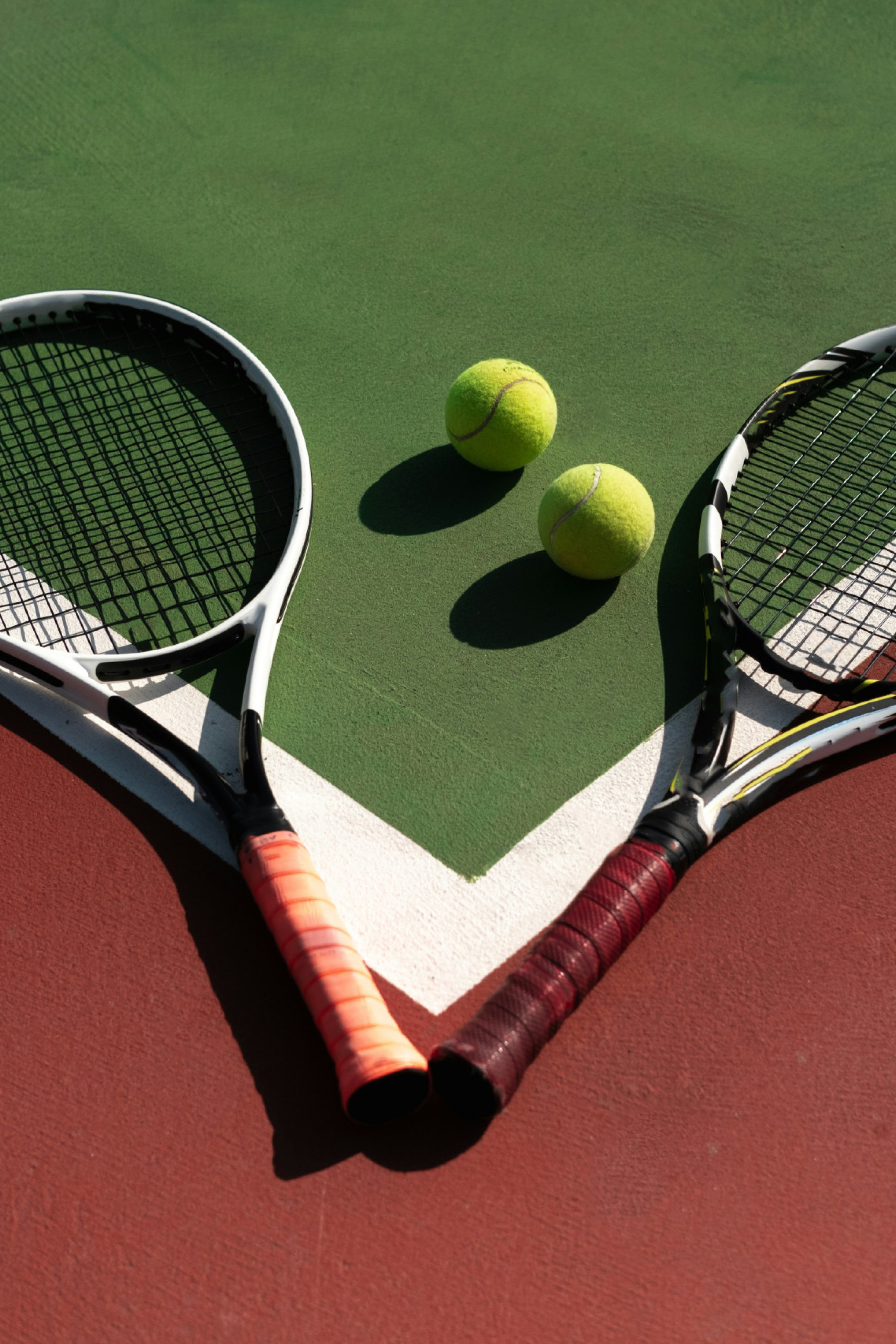 2 tennis rackets and 2 tennis balls sitting on a court