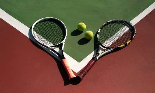 2 tennis rackets and 2 tennis balls sitting on a court.