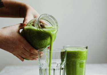 Person pouring green smoothie into glass.