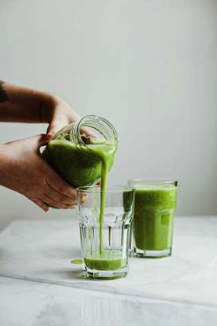 Person pouring green smoothie into glass.