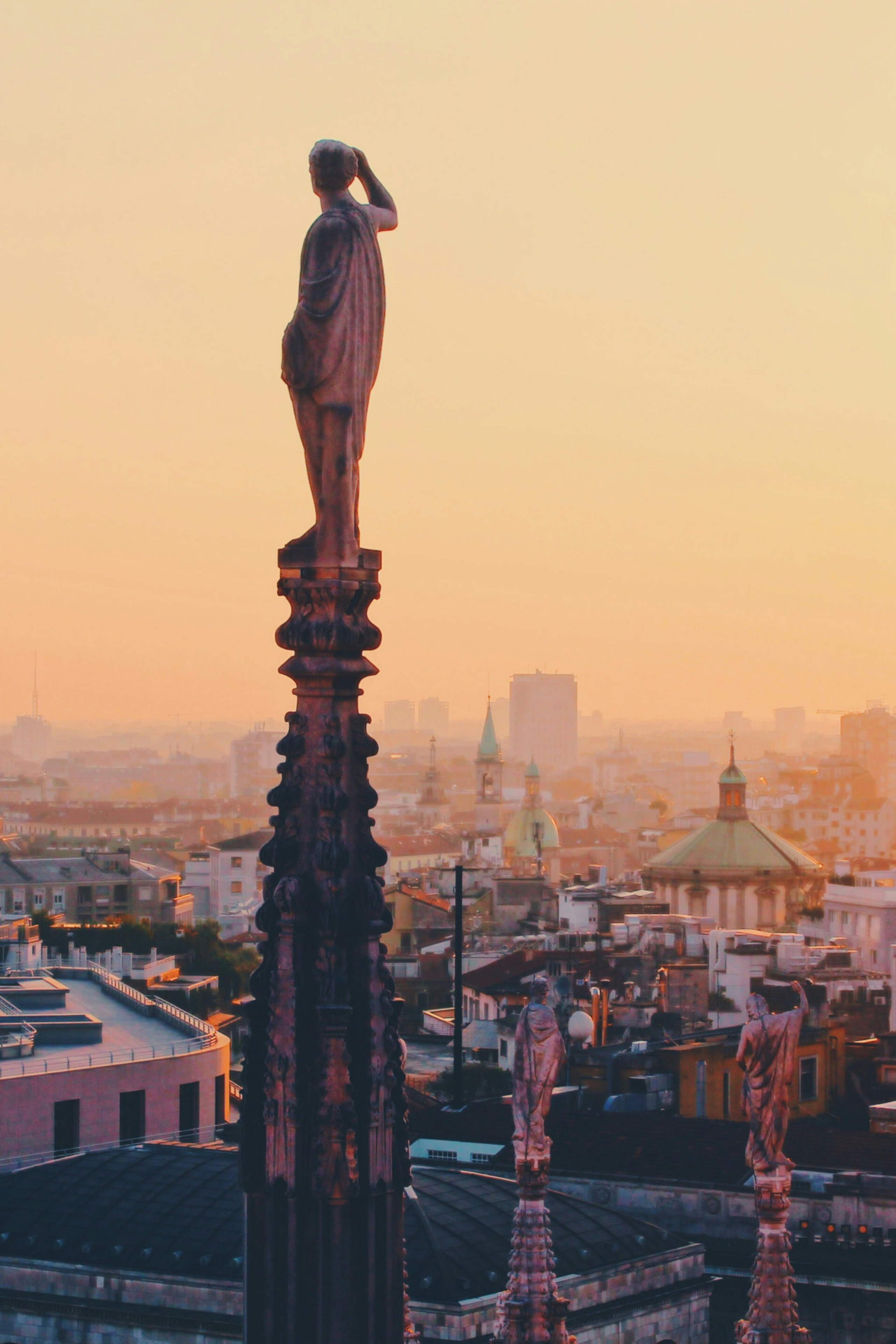 statues atop tall columns with the sunset and Milan in the background