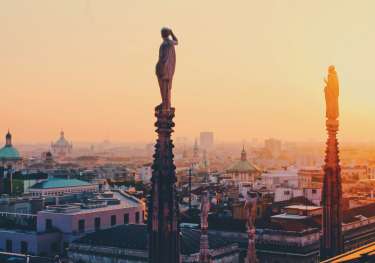 Statues atop tall columns with the sunset and Milan in the background.