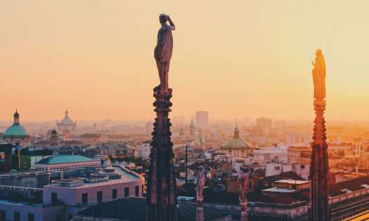 Statues atop tall columns with the sunset and Milan in the background.