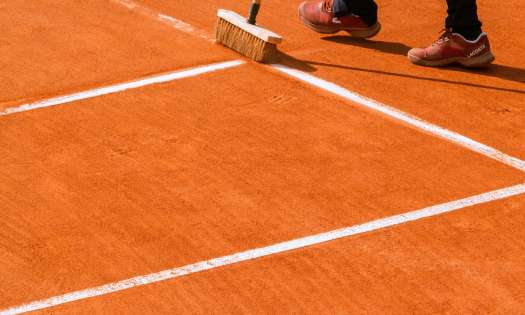 Person brushing red clay tennis court.