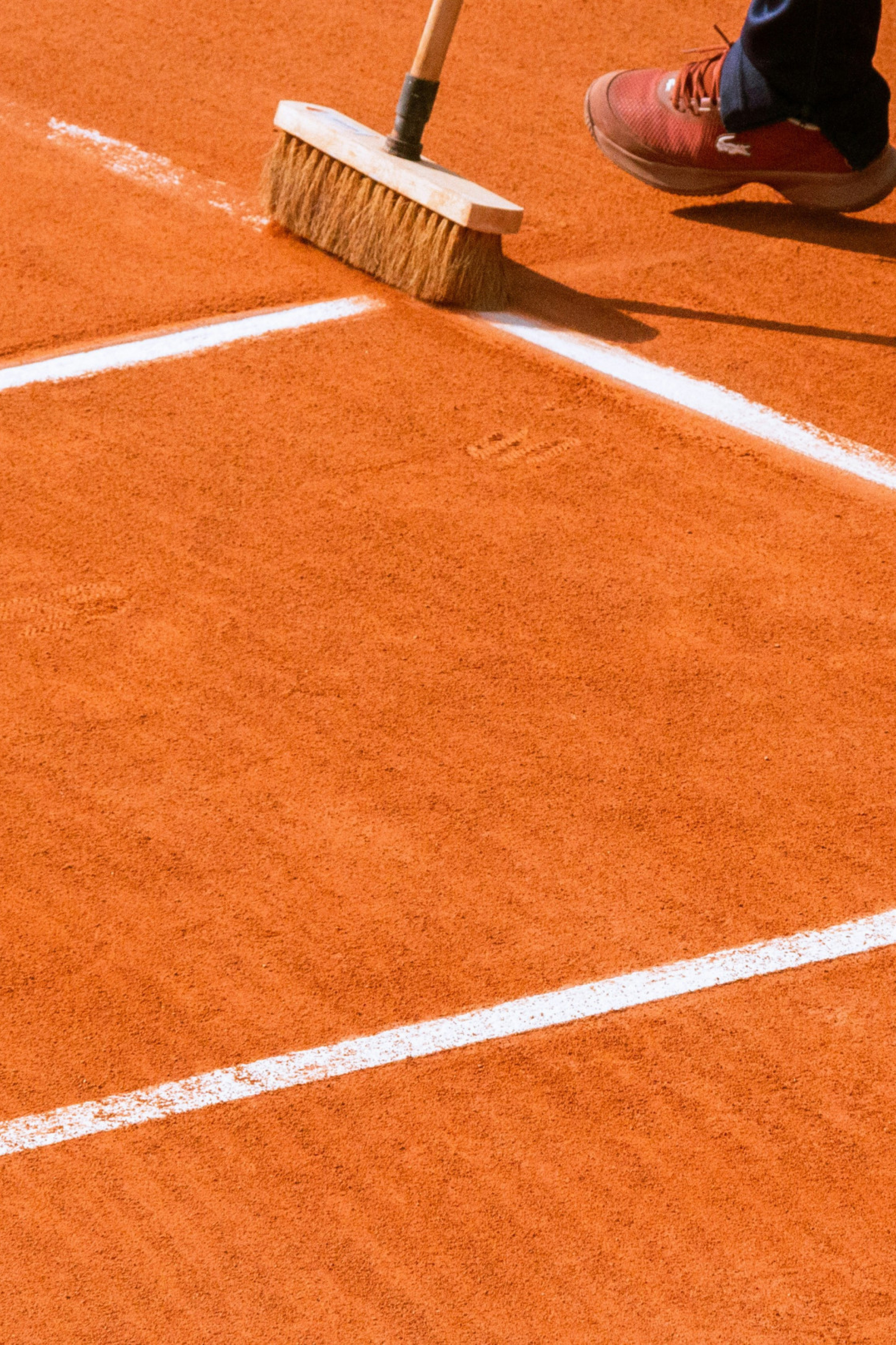person brushing red clay tennis court