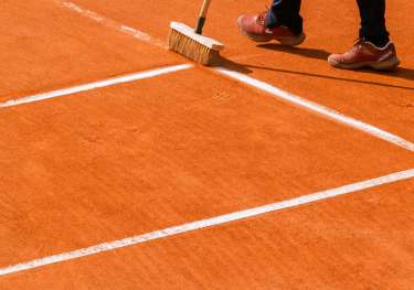 Person brushing red clay tennis court.