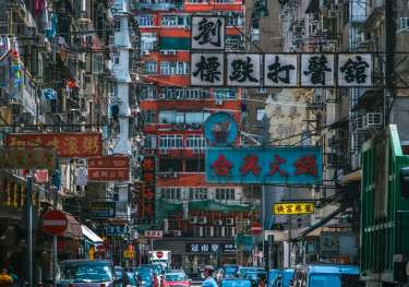 Vibrant street in Hong Kong with signs above and a biker in the middle.