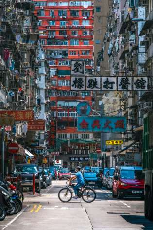 Vibrant street in Hong Kong with signs above and a biker in the middle.
