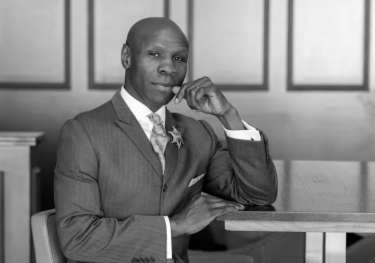 Black and white photo of chris eubank sat at wooden table.