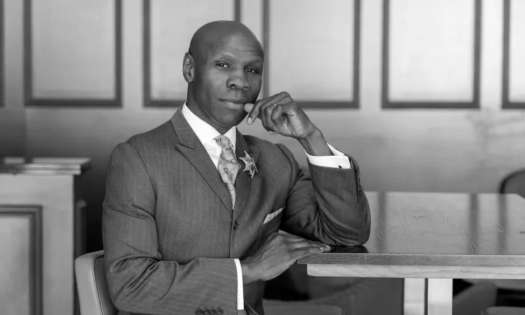Black and white photo of chris eubank sat at wooden table.