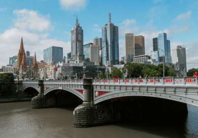 Melbourne city line behind metal and red bridge.