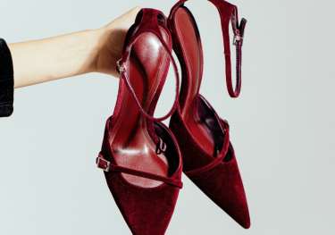 Red shoes held in front of a plain white background.