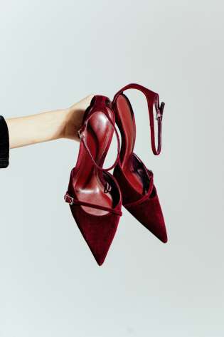 Red shoes held in front of a plain white background.