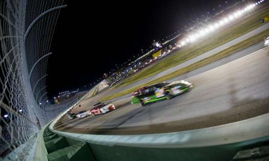 Race cars racing on a track at night in a stadium-like setup.