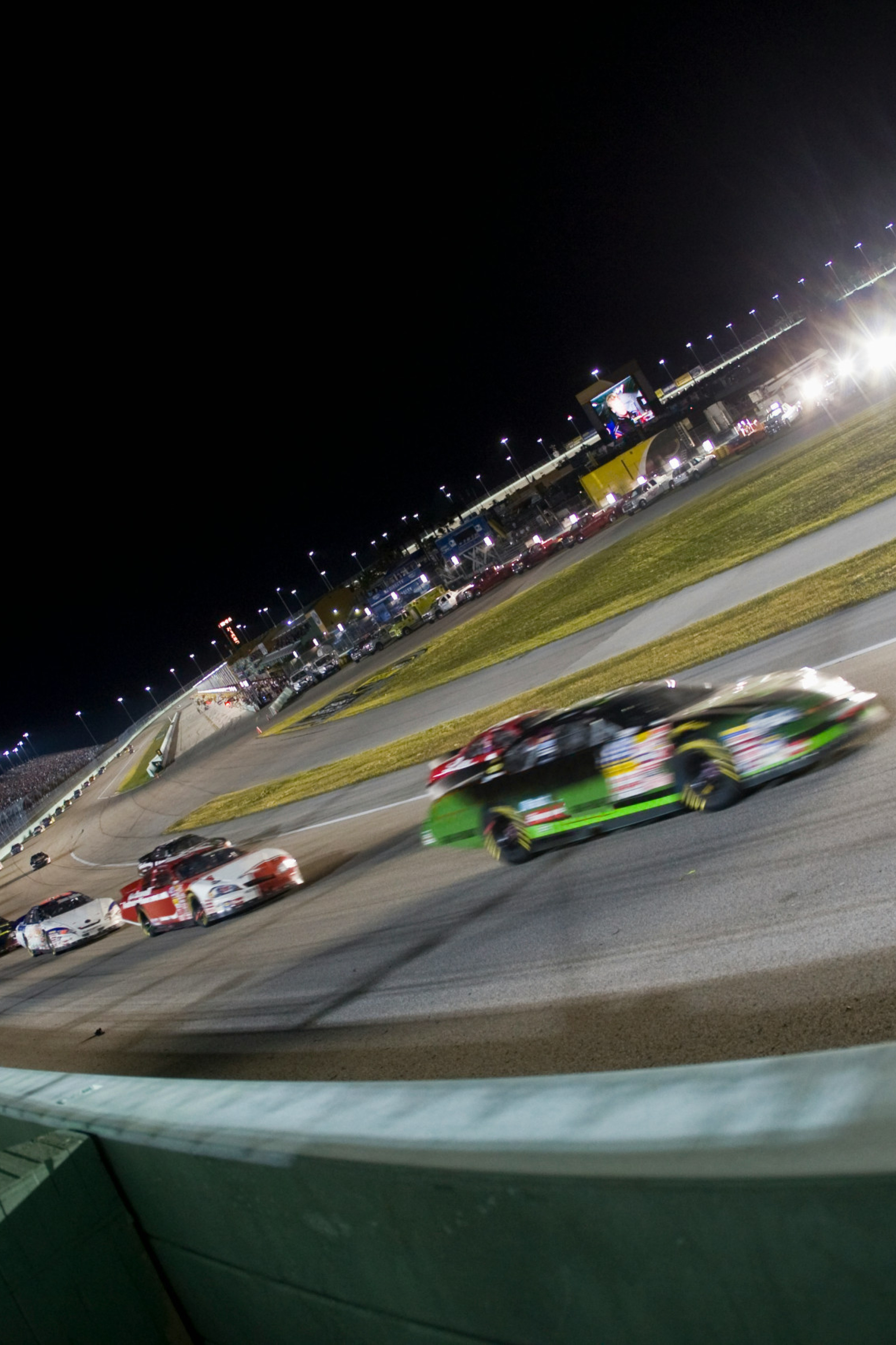 Race cars racing on a track at night in a stadium-like setup