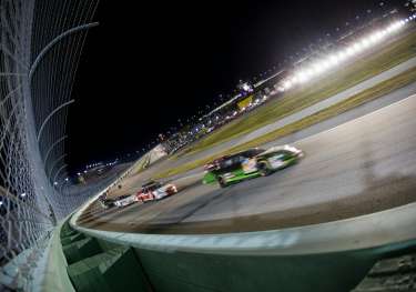 Race cars racing on a track at night in a stadium-like setup.