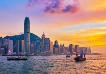 Hong Kong city skyline during sunset with the ocean in front and boats.