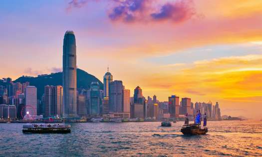 Hong Kong city skyline during sunset with the ocean in front and boats.