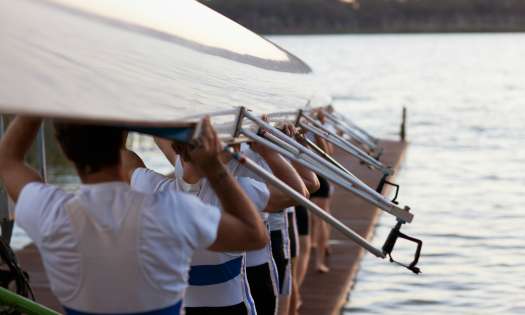 Rowers posing with rowing boat above their heads.