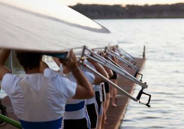 Rowers posing with rowing boat above their heads.