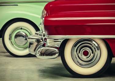 Bumper and wheel of a red vintage car in front of a mint green vintage car.