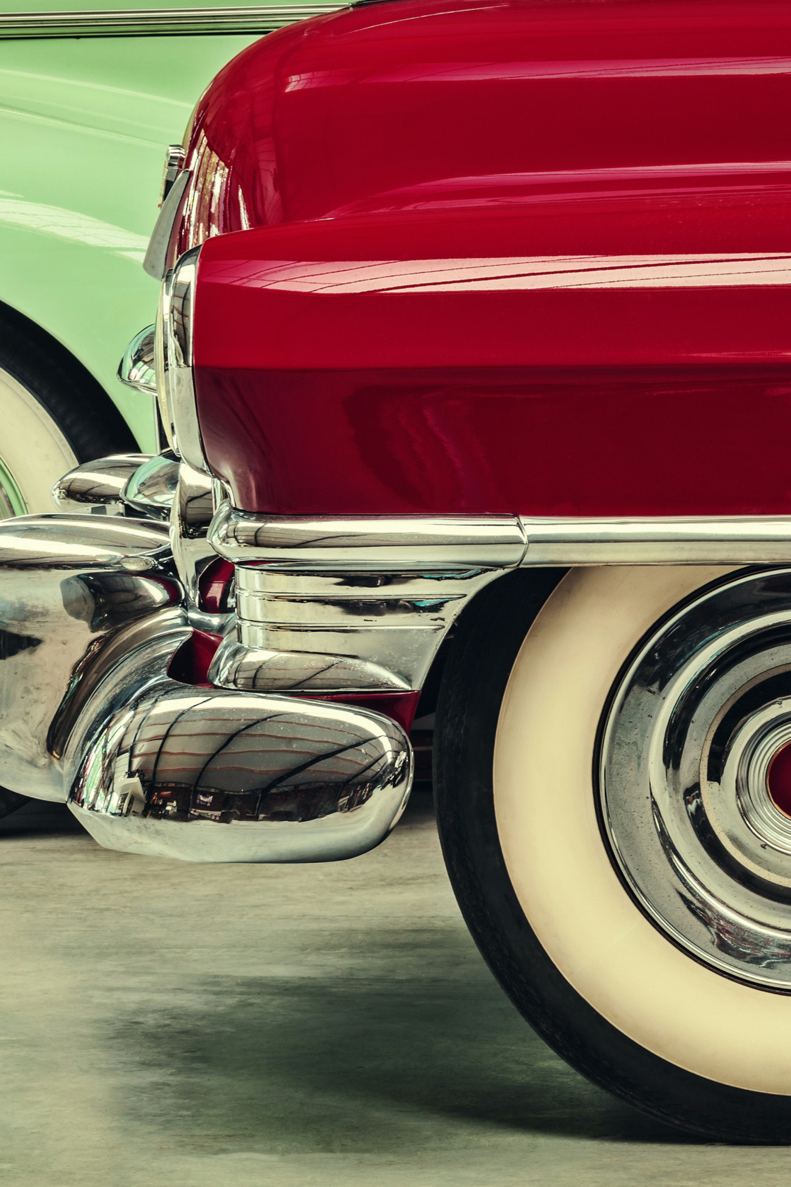 bumper and wheel of a red vintage car in front of a mint green vintage car.