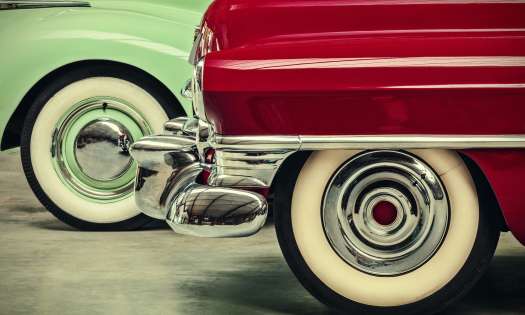Bumper and wheel of a red vintage car in front of a mint green vintage car.
