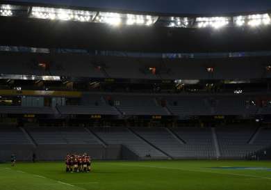 Empty stadium at night with a rugby team huddled on the field.