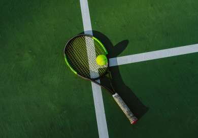 Tennis ball on top of a racket, on a tennis court.