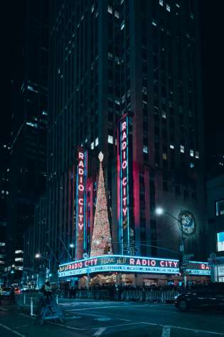 Neon Radio City lights and a Christmas tree in front of a skyscraper.