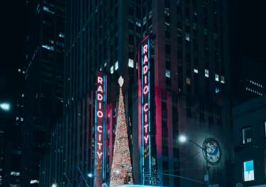 Neon Radio City lights and a Christmas tree in front of a skyscraper.